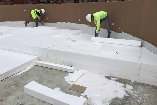 Two construction workers lay geofoam at the base of a pool