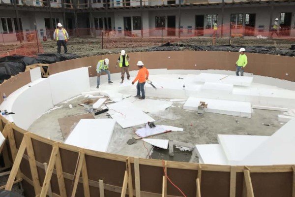 Four construction workers stand within a pool being constructed among sheets of geofoam